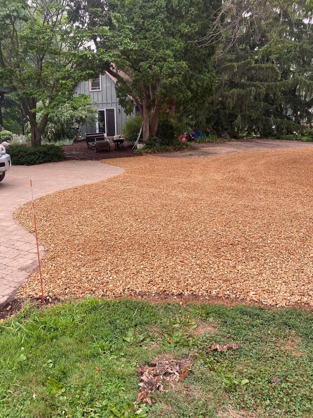 Gravel driveway update with new stone layer around green landscaping and patio area.