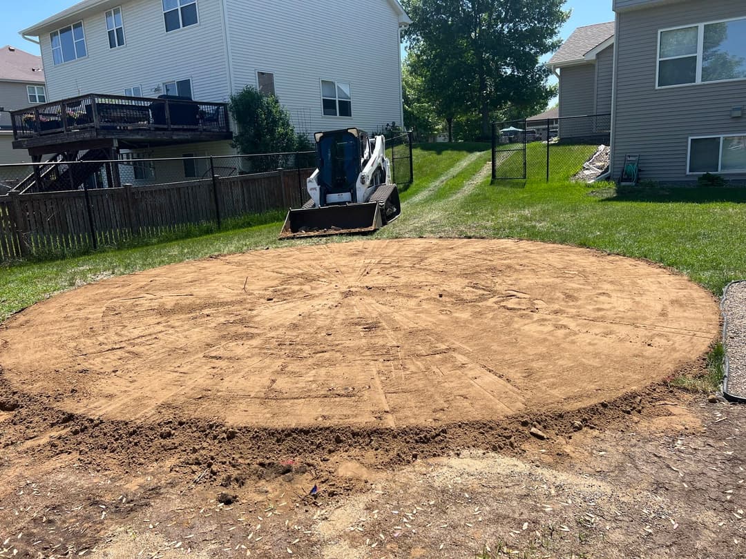 Excavated circular area in backyard with skid steer loader and nearby houses.